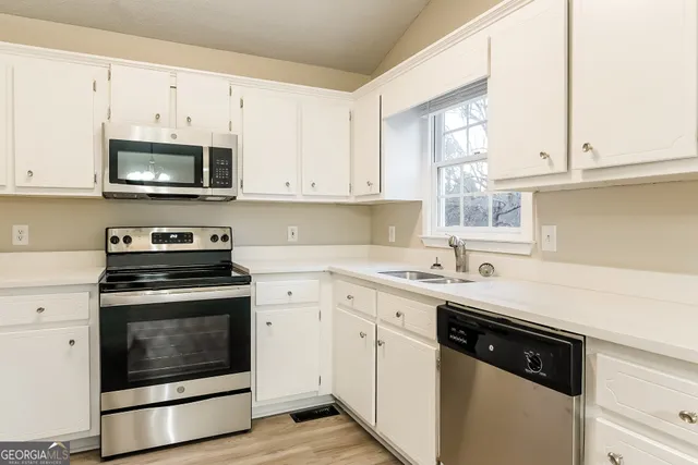 a kitchen with stainless steel appliances granite countertop white cabinets a sink a stove a microwave and oven with white cabinets