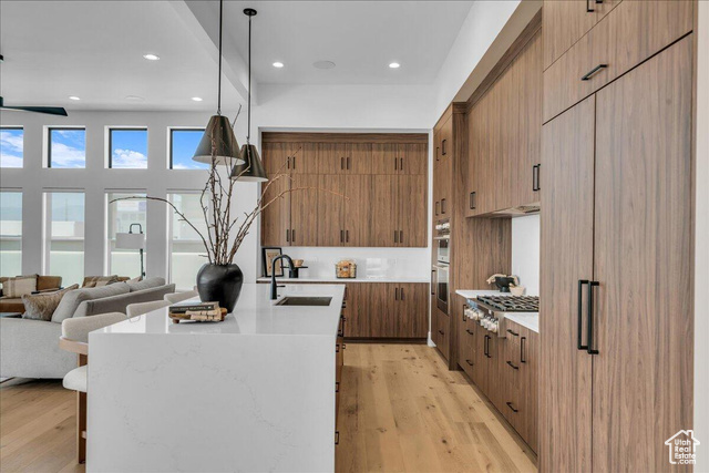 2761 West Lava Hls Road Santa Clara, UT 84765 - Photo 7 of 53 Kitchen with light stone countertops, light wood-style floors, brown cabinetry, a center island with sink, and decorative light fixtures