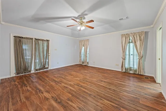 an empty room with wooden floor fan and windows