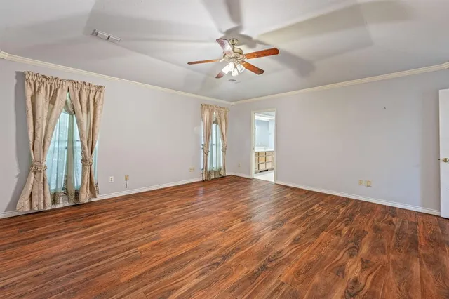 a view of an empty room with wooden floor and a ceiling fan