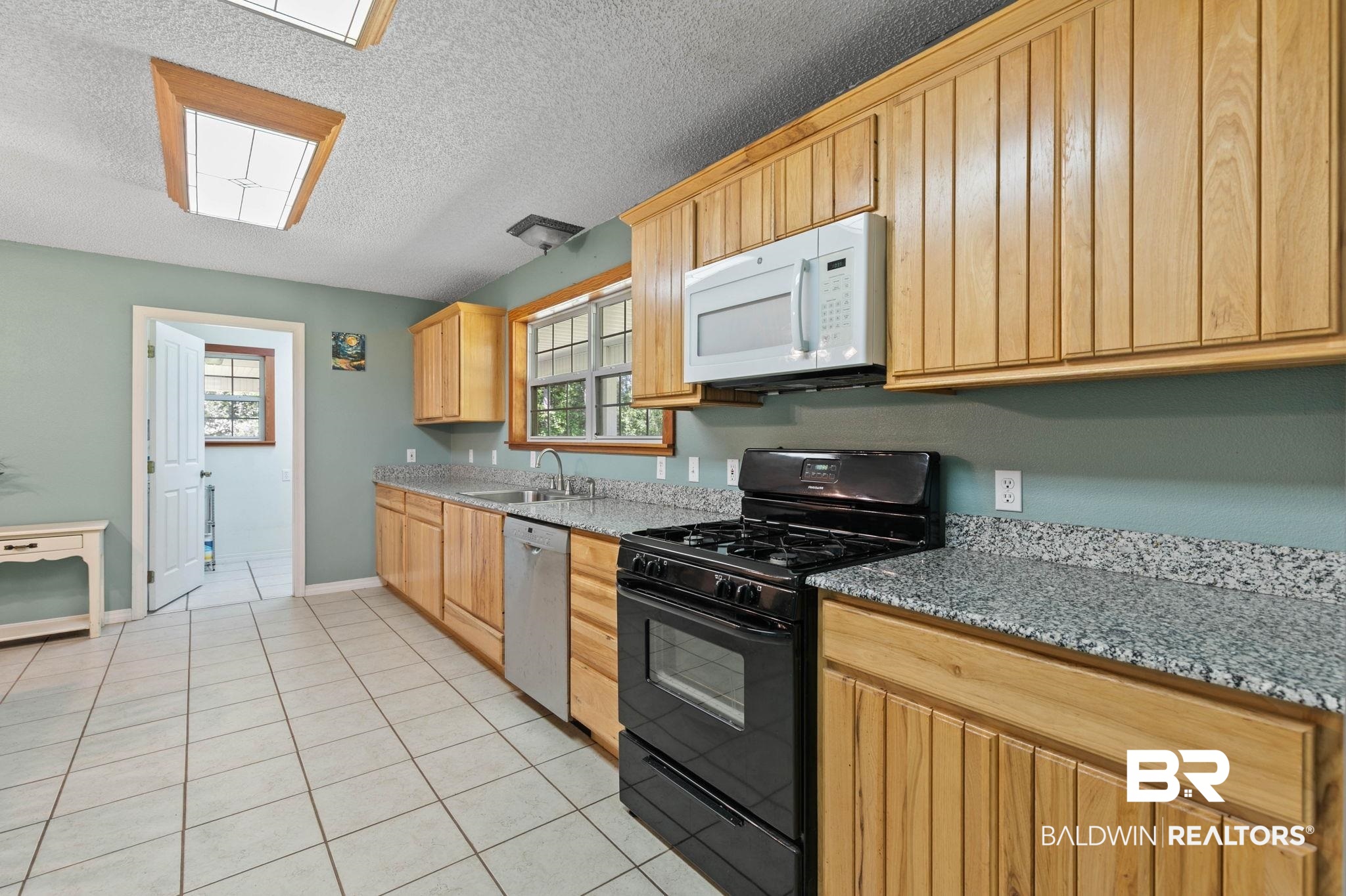 20219 Greek Cemetery Road Robertsdale, AL 36567 - Photo 17 of 41 Kitchen featuring light wood cabinetry, granite-finish countertops, stainless-steel dishwasher, black gas range, and white tile flooring