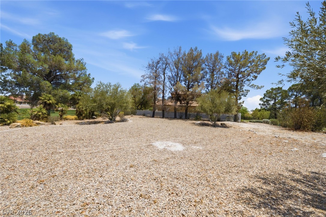 20 Innisbrook Avenue Las Vegas, NV 89113 - Photo 13 of 39 A spacious gravel lot with mature trees and a distant structure provides a serene setting.