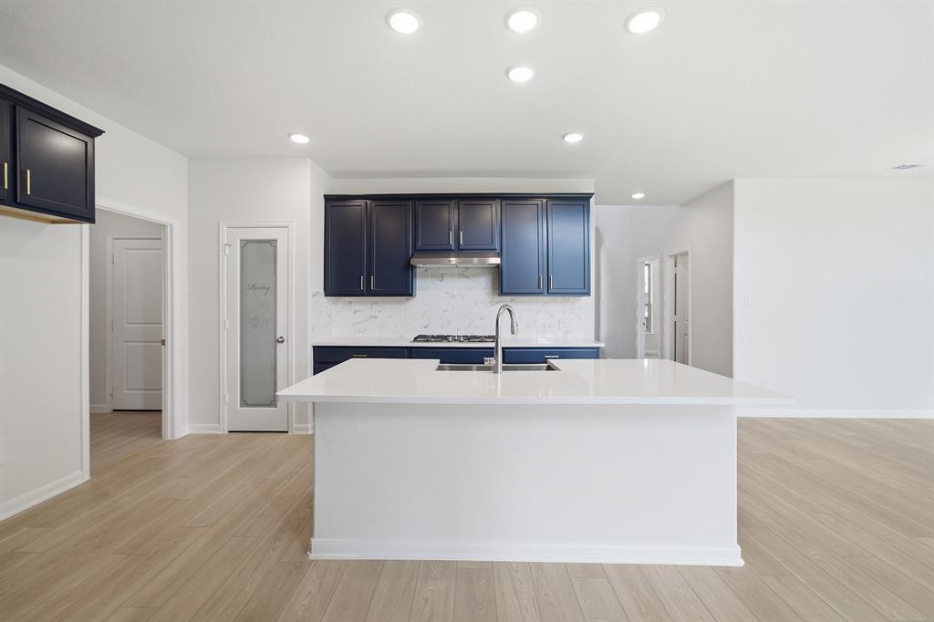 1908 Sangallo Lane Celina, TX 75009 - Photo 22 of 35 Open-concept kitchen featuring a large island with an undermount sink, dark blue cabinetry, white countertops, and wood-finish flooring