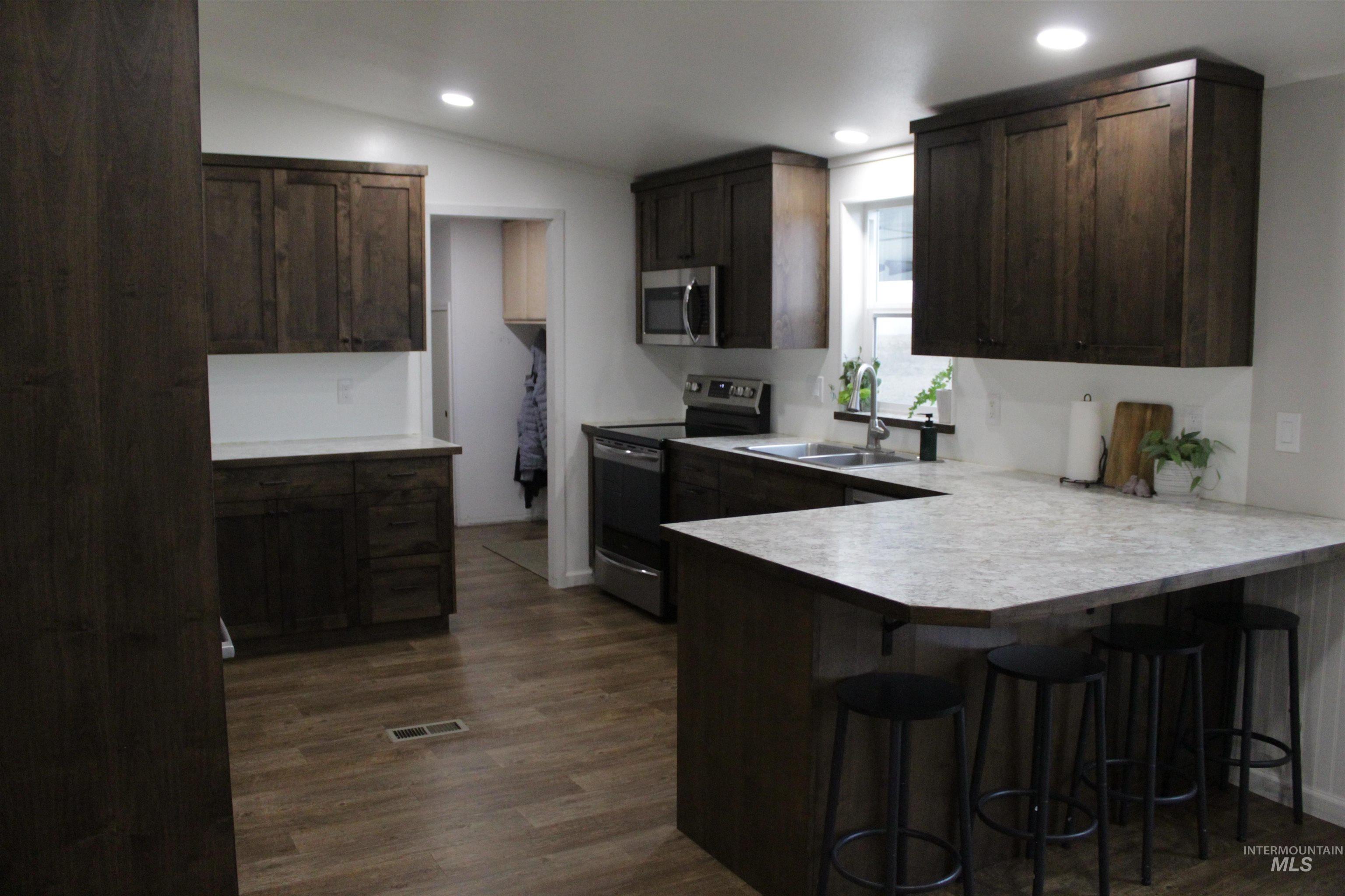27520 Pearl Road Parma, ID 83660 - Photo 4 of 29 Kitchen with dark wood finish cabinets, stainless steel appliances, light countertops, a peninsula, and dark wood finished floors