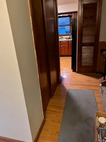 a view of a hallway to an empty room with wooden floor and a kitchen