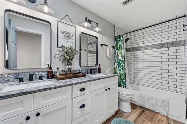 a bathroom with a double vanity sink a toilet a mirror and shower