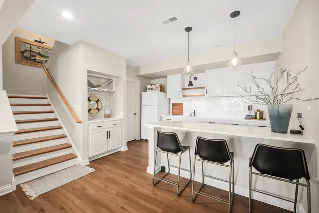 a kitchen with stainless steel appliances kitchen island granite countertop a sink a stove a refrigerator and white cabinets with wooden floor