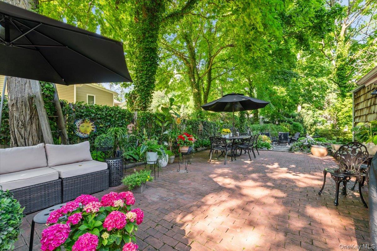 10 Rancher Place Huntington, NY 11743 - Photo 31 of 44 Spacious brick paver patio featuring mature trees, lush perimeter landscaping, a privacy hedge, and a shingle-sided exterior