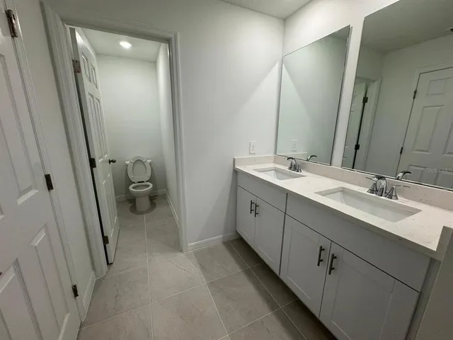 a bathroom with a double vanity sink and mirror with toilet