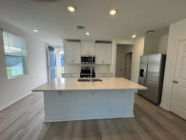 a large kitchen with stainless steel appliances a large counter top a stove and a refrigerator