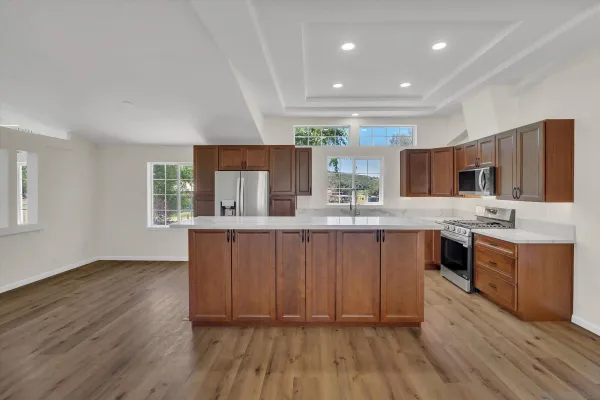 a kitchen with stainless steel appliances kitchen island granite countertop wooden floors wooden cabinets and sink