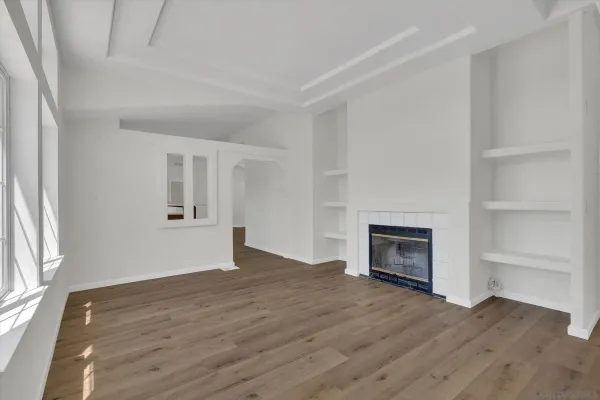 an empty room with wooden floor fireplace and windows