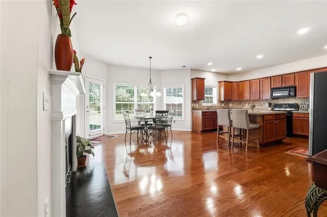 a kitchen with stainless steel appliances granite countertop a refrigerator a stove top oven a dining table and chairs with wooden floor