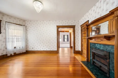 a view of an empty room with wooden floor fireplace and a window
