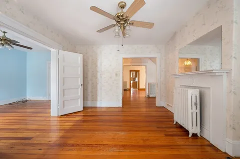 a view of a livingroom with wooden floor a ceiling fan and windows