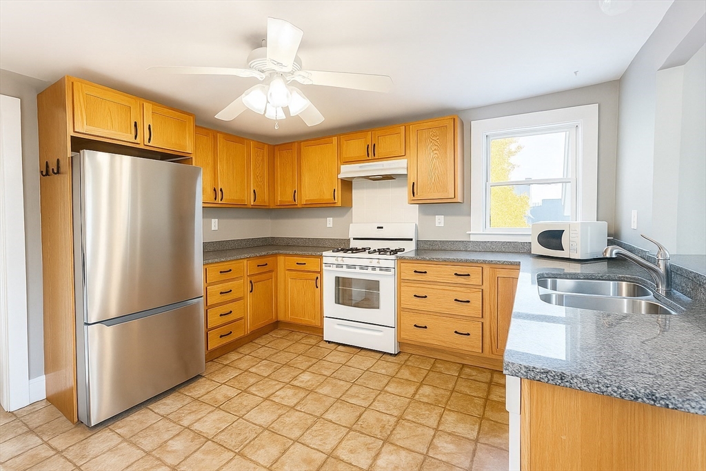 133 Brattle Street, Unit 2 Arlington, MA 02474 - Photo 2 of 15 a kitchen with granite countertop a refrigerator a sink dishwasher a stove and white cabinets with wooden floor