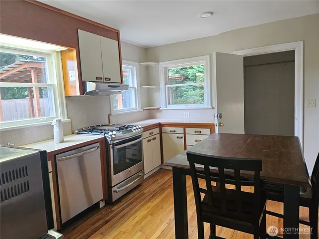 a kitchen with stainless steel appliances granite countertop a stove a sink dishwasher a dining table and chairs with wooden floor