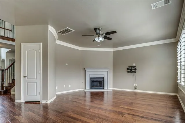 a view of an empty room with wooden floor and a ceiling fan