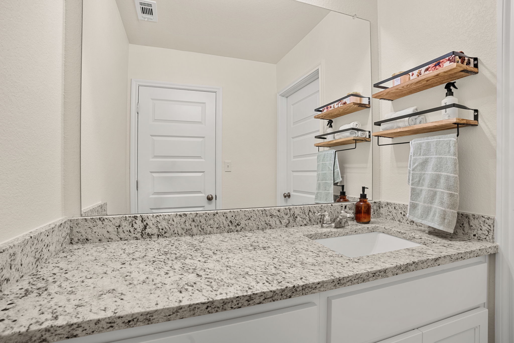 148 Hidalgo Lane Elgin, TX 78621 - Photo 28 of 38 A well-lit bathroom vanity features a granite countertop and contemporary shelving.
