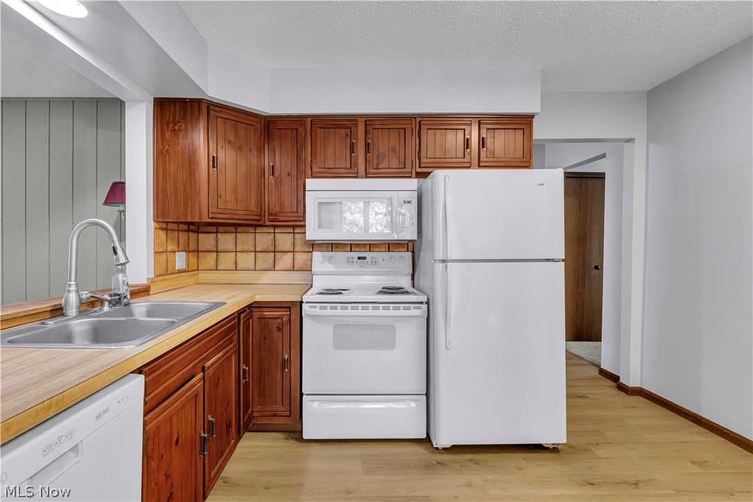 6635 Taylor Road Painesville, OH 44077 - Photo 19 of 41 Kitchen featuring wood-finish flooring, wood cabinetry, stainless steel double-basin sink with gooseneck faucet, white appliances including a refrigerator, range, and microwave, and square tile backsplash