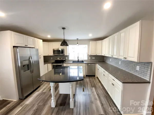 a kitchen with stainless steel appliances granite countertop a refrigerator a stove top oven a sink dishwasher and white cabinets with wooden floor