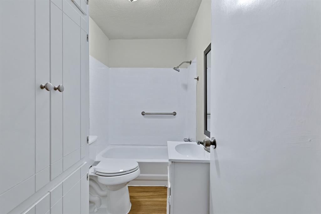 613 Cheyenne Road Dallas, TX 75217 - Photo 22 of 28 Bathroom featuring a white vanity with integrated sink, a built-in bathtub with shower, a chrome showerhead, and wood-finish flooring