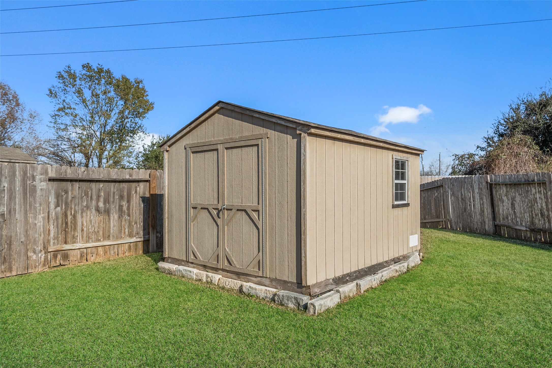4747 Abercorn Street Rosharon, TX 77583 - Photo 36 of 46 This photo shows a well-maintained backyard featuring a sturdy wooden shed with double doors, set on a stone foundation. It's surrounded by a wooden privacy fence, offering ample outdoor storage space.
