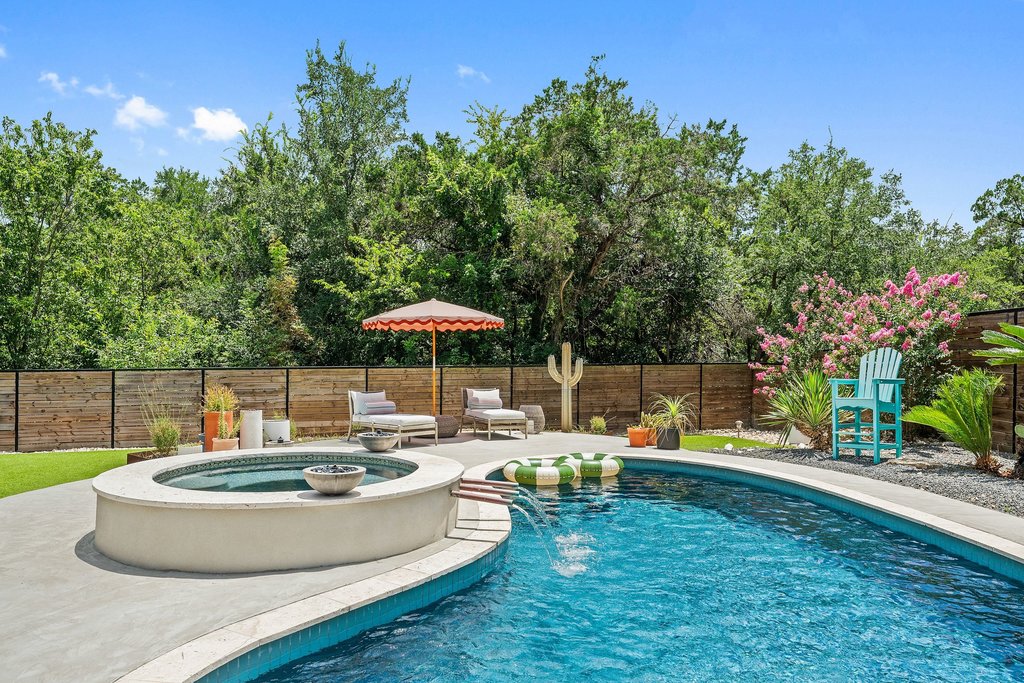 6017 Open Range Trail Austin, TX 78749 - Photo 1 of 1 A private backyard oasis features a shimmering pool and an integrated spa, encircled by a natural wood fence and mature trees.