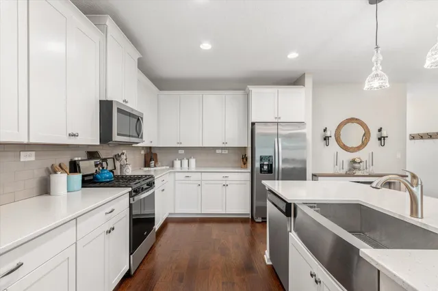 a kitchen with a sink dishwasher a stove top oven a refrigerator with white cabinets and wooden floor