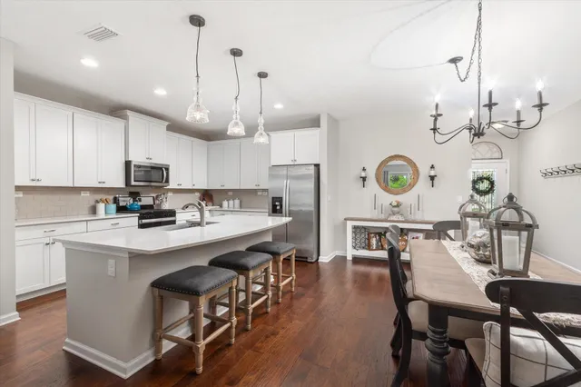 a kitchen with a dining table chairs stove and white cabinets with wooden floor
