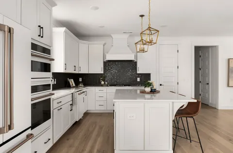 a kitchen with stainless steel appliances a stove a sink dishwasher a refrigerator white cabinets and wooden floor