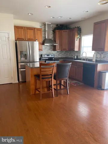 a kitchen with stainless steel appliances kitchen island granite countertop a refrigerator a stove a sink a dining table and chairs with wooden floor