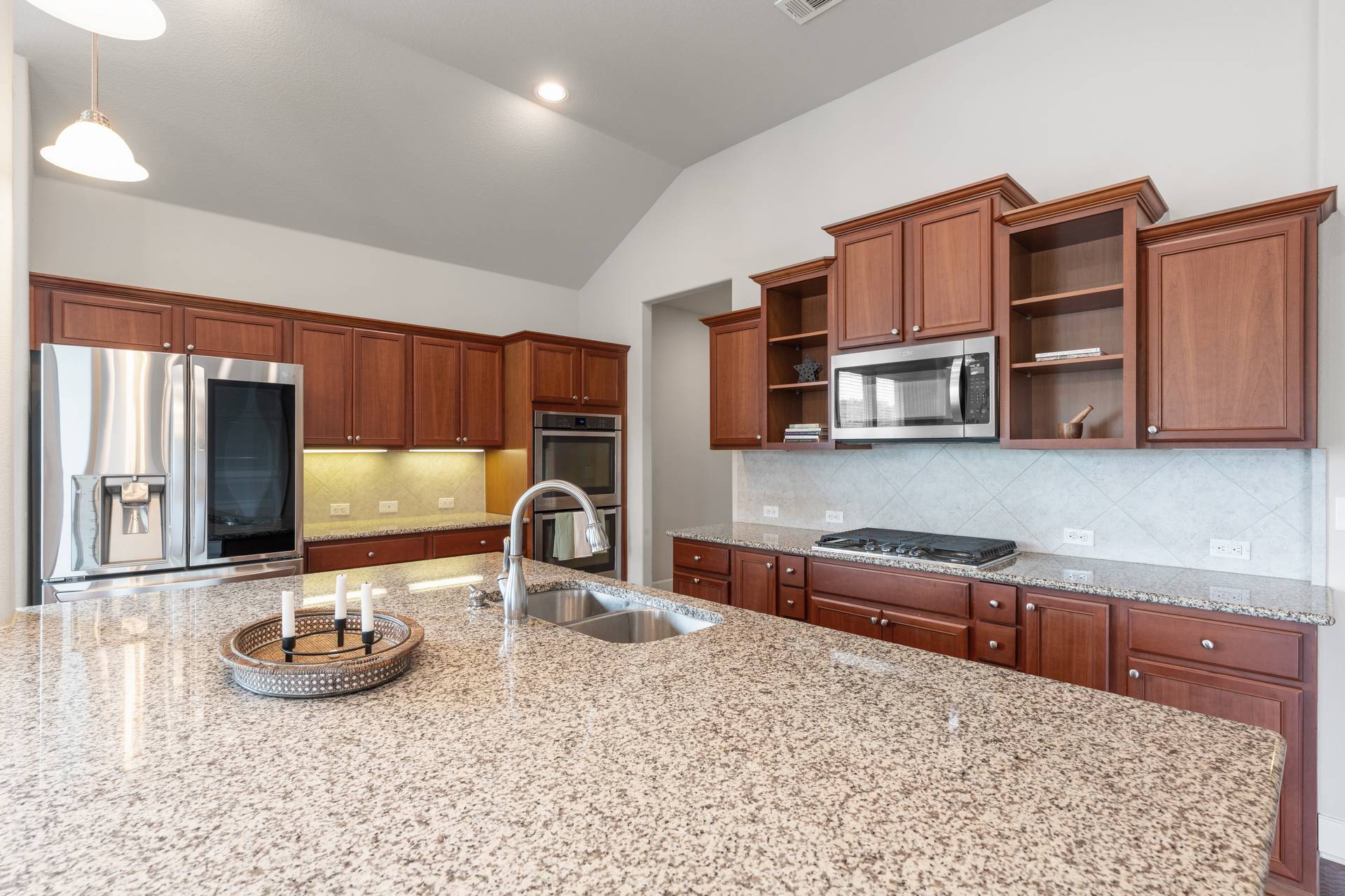 3516 Venezia View Leander, TX 78641 - Photo 26 of 40 Kitchen featuring stainless steel appliances, light stone counters, backsplash, vaulted ceiling, and wood finish cabinetry