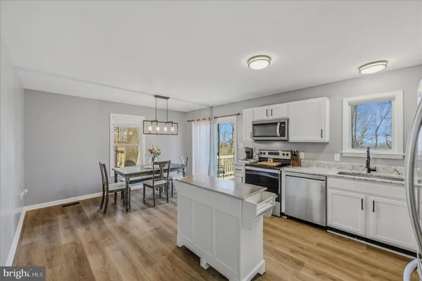 a kitchen with stainless steel appliances granite countertop a stove top oven a sink a dining table and chairs with wooden floor