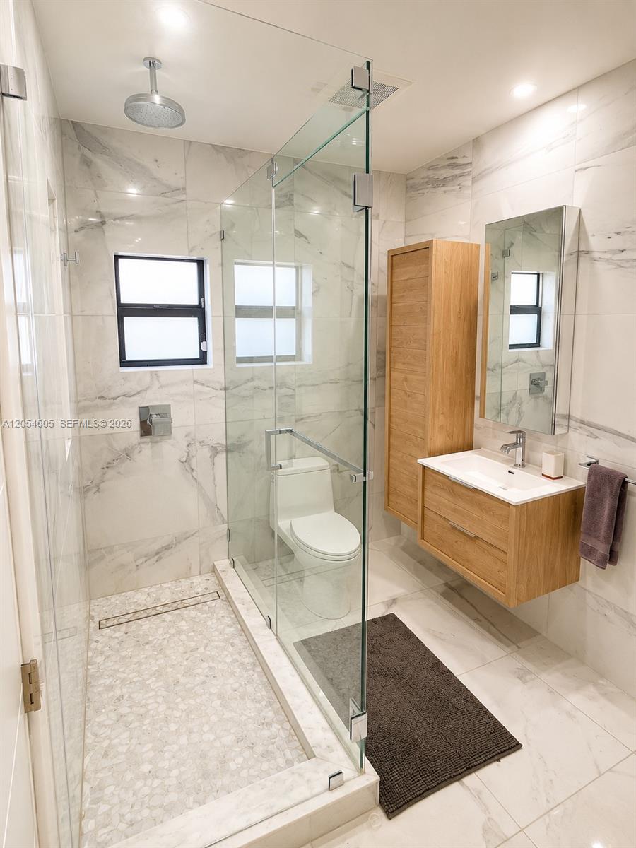 3538 Southwest 1st Avenue, Unit 1 Miami, FL 33145 - Photo 13 of 20 Beautifully renovated full bathroom featuring floor-to-ceiling marble-look tile, a frameless glass walk-in shower, modern floating vanity with abundant storage, and premium contemporary fixtures. Bright, elegant, and thoughtfully designed, this bathroom combines clean lines with spa-inspired finishes, creating a luxurious and comfortable space for family or guests.