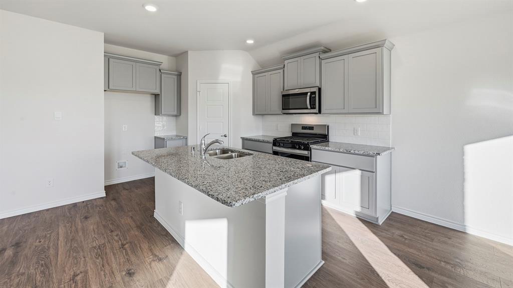 419 Epiphany Lane Lavon, TX 75166 - Photo 3 of 31 Kitchen featuring a center island with double basin sink, stainless steel appliances, light gray cabinetry, and granite countertops