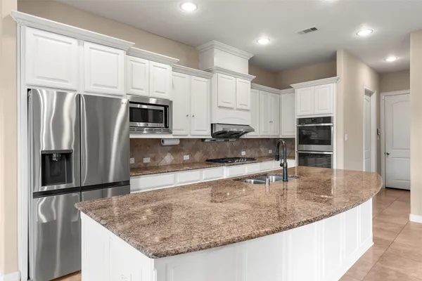 a kitchen with stainless steel appliances granite countertop a refrigerator a oven a sink and white cabinets
