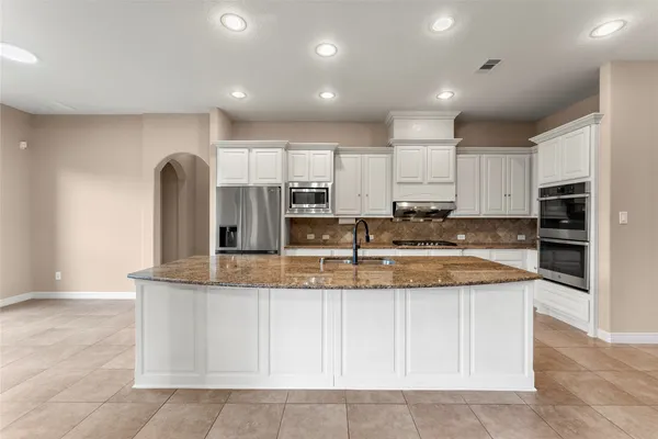 a large kitchen with granite countertop a sink and white cabinets