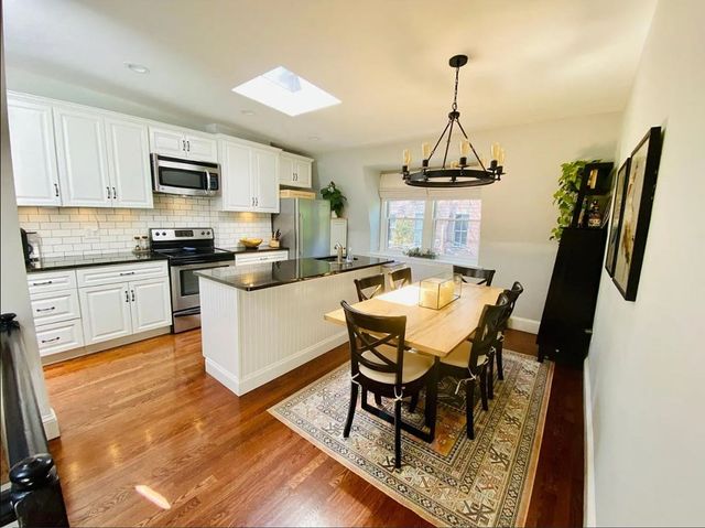 a kitchen with stainless steel appliances a stove a sink dishwasher a dining table and chairs with wooden floor