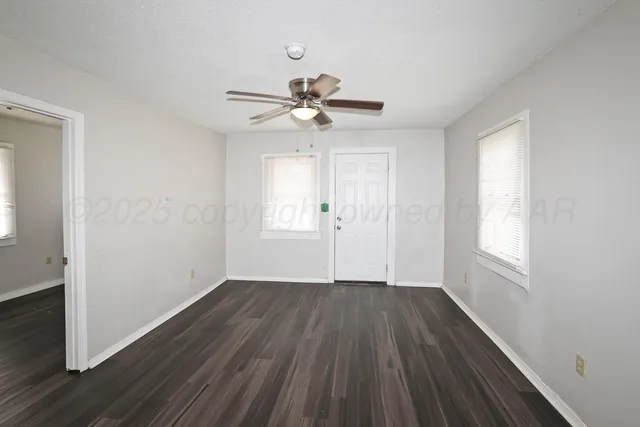 an empty room with wooden floor ceiling fan and windows