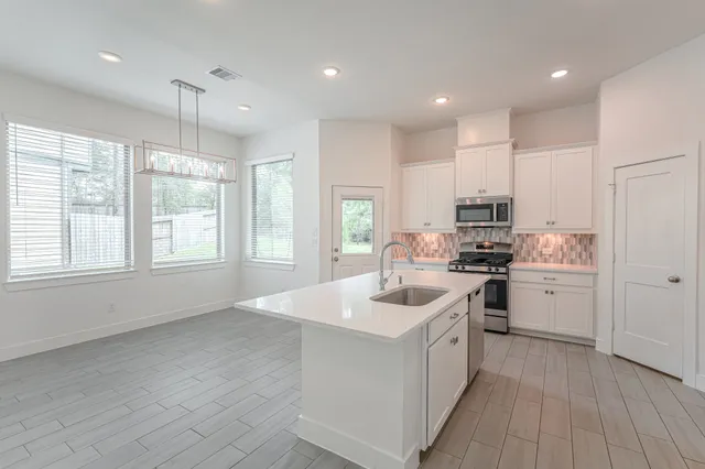 a kitchen with stove a sink dishwasher a refrigerator and white cabinets with wooden floor