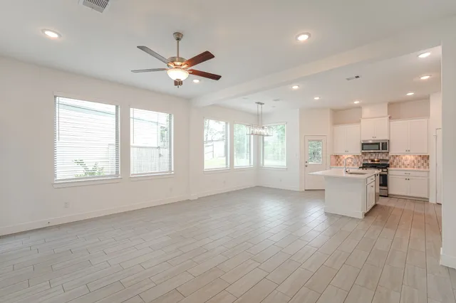 a view of an empty room and kitchen with wooden floor and a window