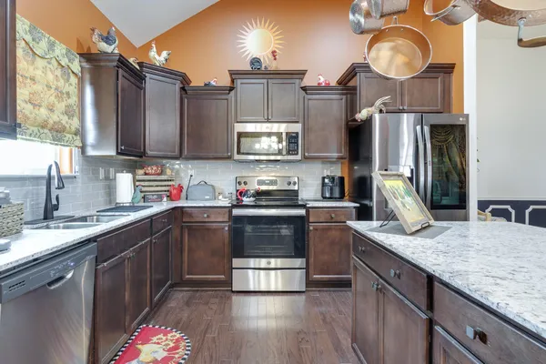 a kitchen with stainless steel appliances granite countertop a sink a stove top oven a clock and cabinets