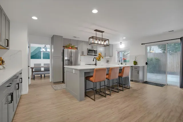a dining hall with stainless steel appliances a table chairs refrigerator and a kitchen view