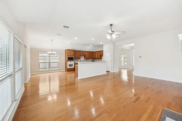 a view of an empty room and kitchen with wooden floor