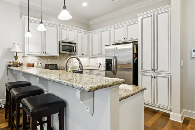 a kitchen with granite countertop a refrigerator a stove a sink and white cabinets with wooden floor