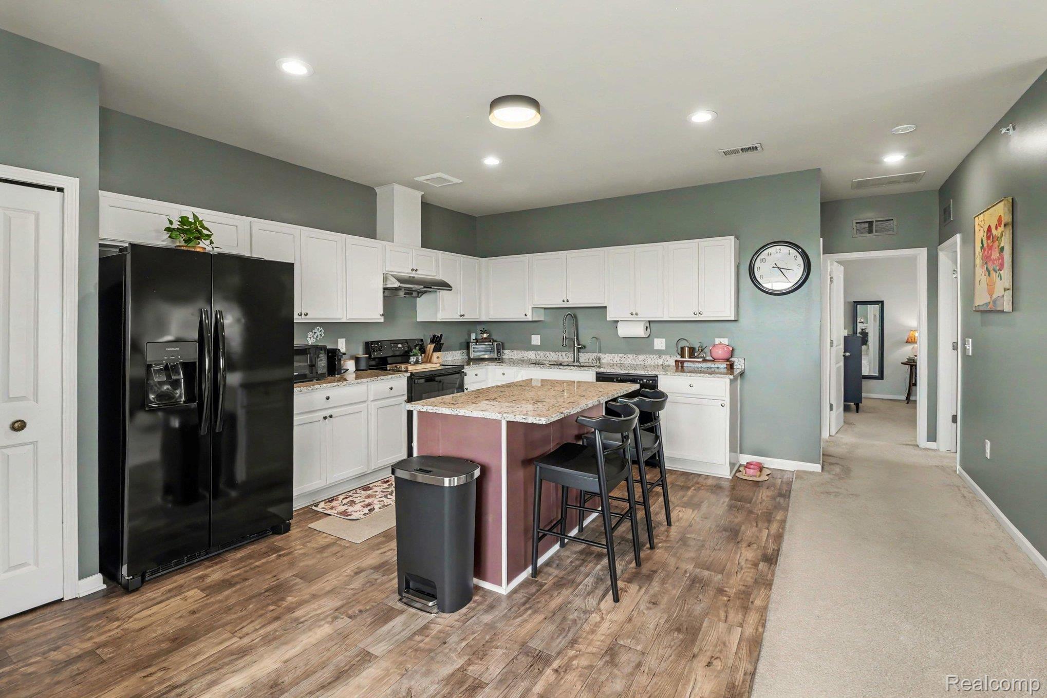 9864 Ridge Run Street Howell, MI 48855 - Photo 13 of 23 Two tone kitchen with black refrigerator with ice dispenser, light stone counters, a kitchen island, a breakfast bar, and dark wood finished floors