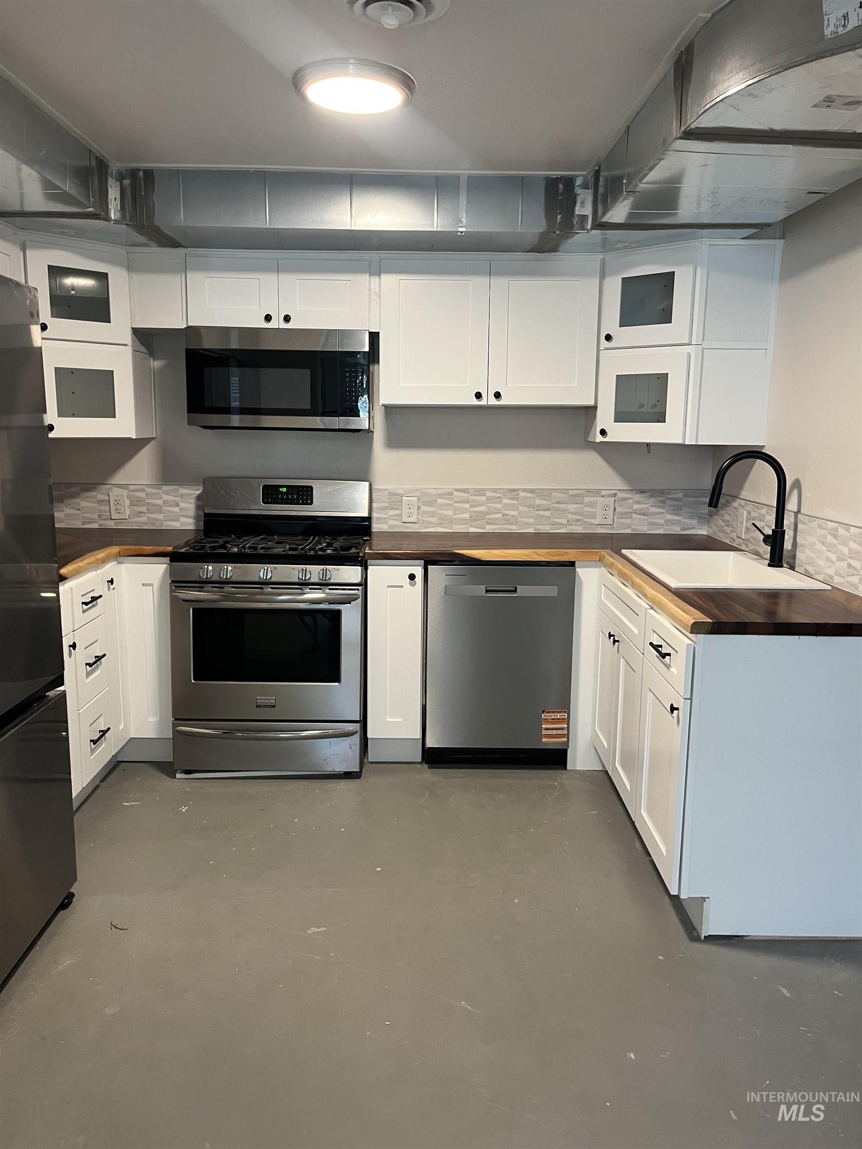1024 El Cajon Street Moscow, ID 83843 - Photo 29 of 49 Kitchen featuring wooden counters, stainless steel appliances, concrete floors, white cabinets, and decorative backsplash