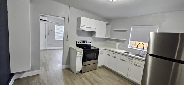 a kitchen with stainless steel appliances a refrigerator a stove a sink and white cabinets with wooden floor