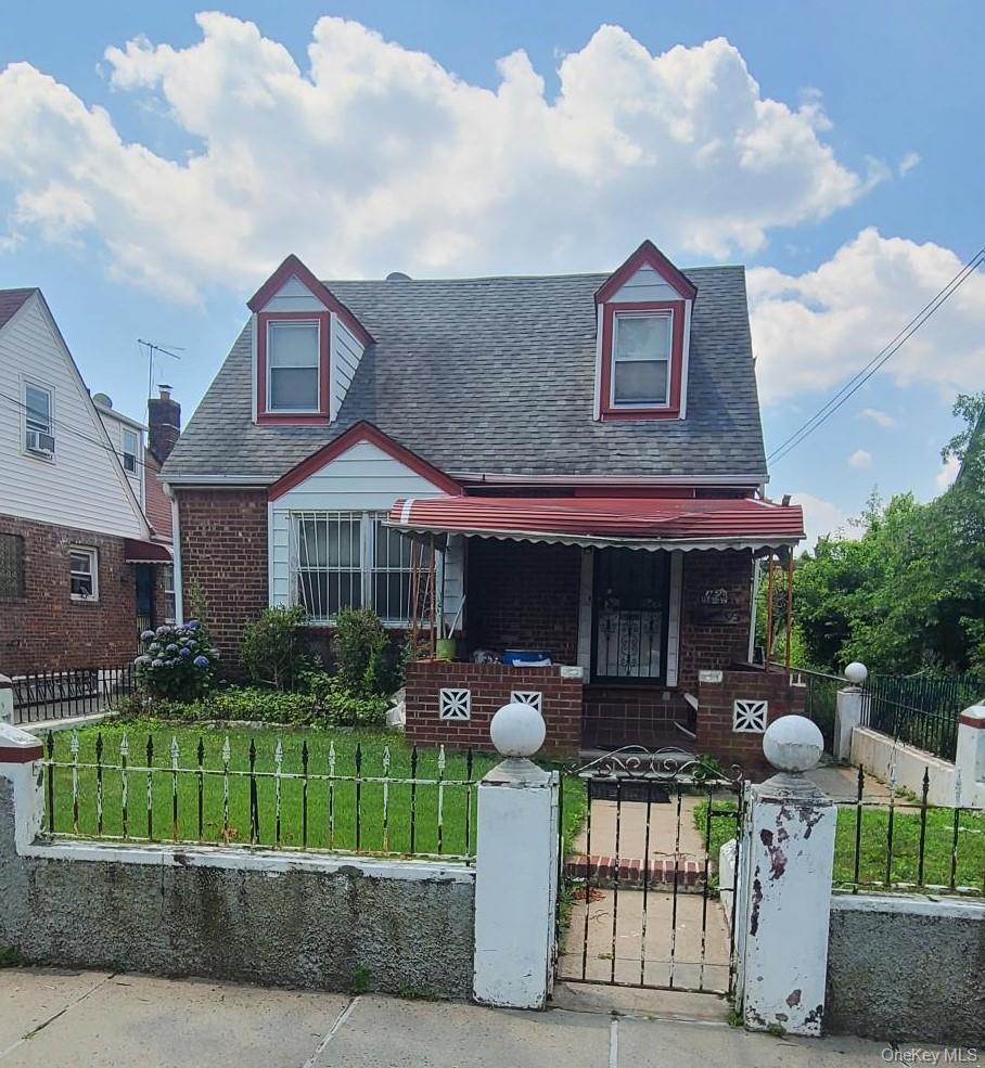 View of front of property with covered porch, brick siding, roof with shingles, and a fenced front yard